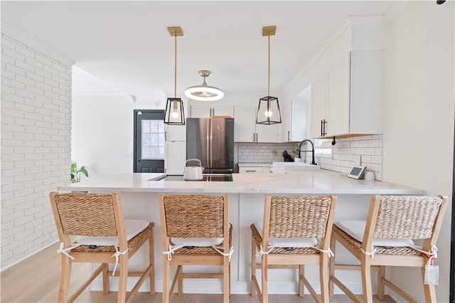 kitchen featuring white cabinetry, sink, stainless steel fridge, hanging light fixtures, and kitchen peninsula