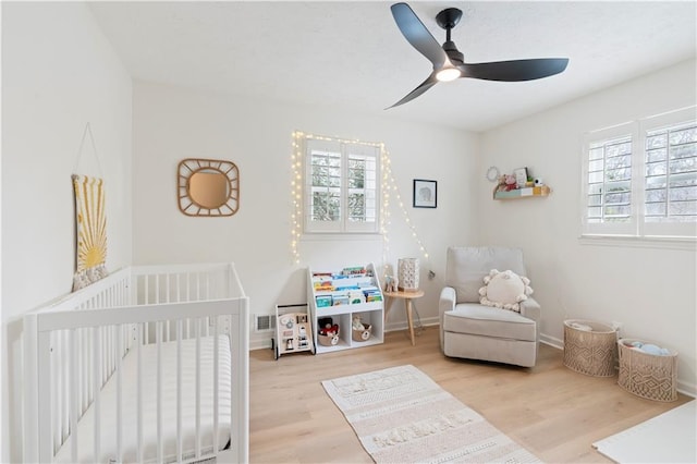 bedroom featuring a crib, light hardwood / wood-style floors, and ceiling fan