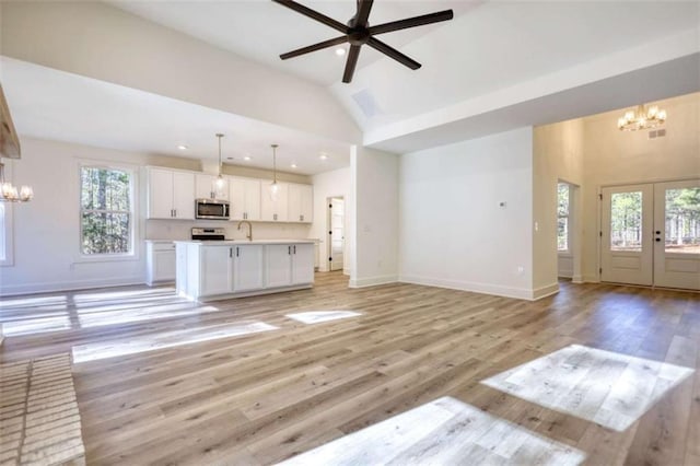 unfurnished living room featuring sink, ceiling fan with notable chandelier, a healthy amount of sunlight, and light wood-type flooring