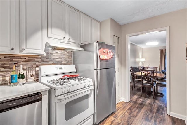 kitchen featuring under cabinet range hood, dark wood-type flooring, white cabinetry, appliances with stainless steel finishes, and backsplash