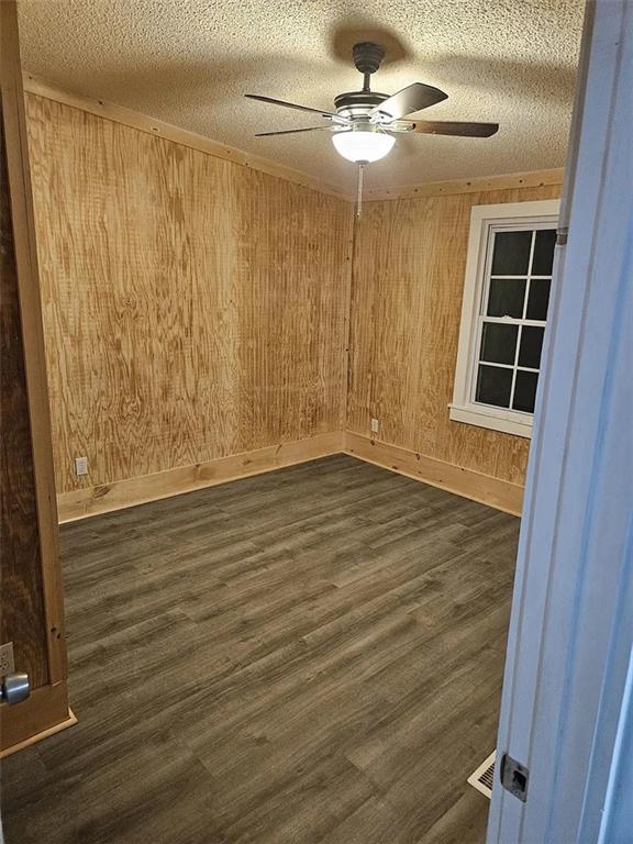 empty room featuring wooden walls, ceiling fan, dark hardwood / wood-style floors, and a textured ceiling