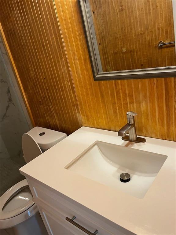 bathroom with vanity, wood walls, and toilet