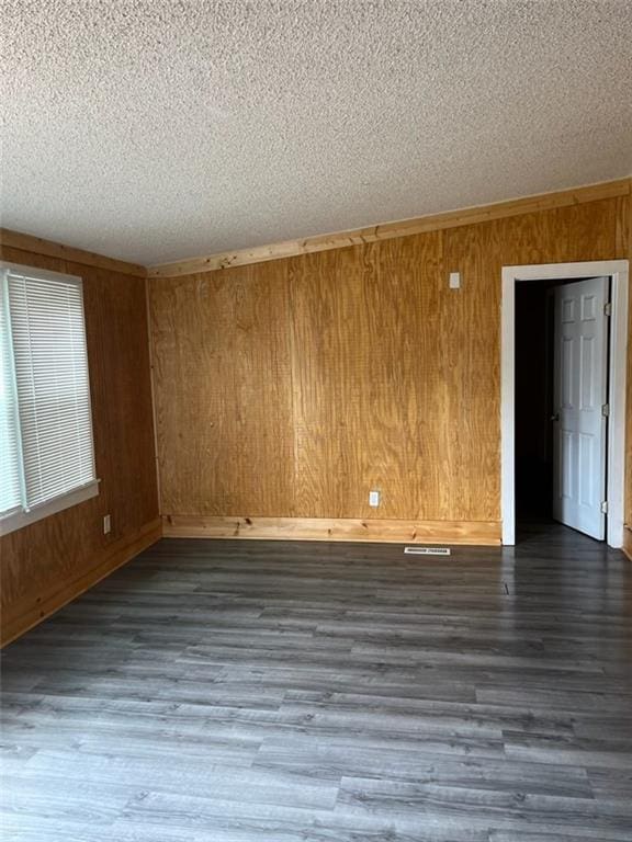 empty room with a textured ceiling, wood walls, and dark wood-type flooring