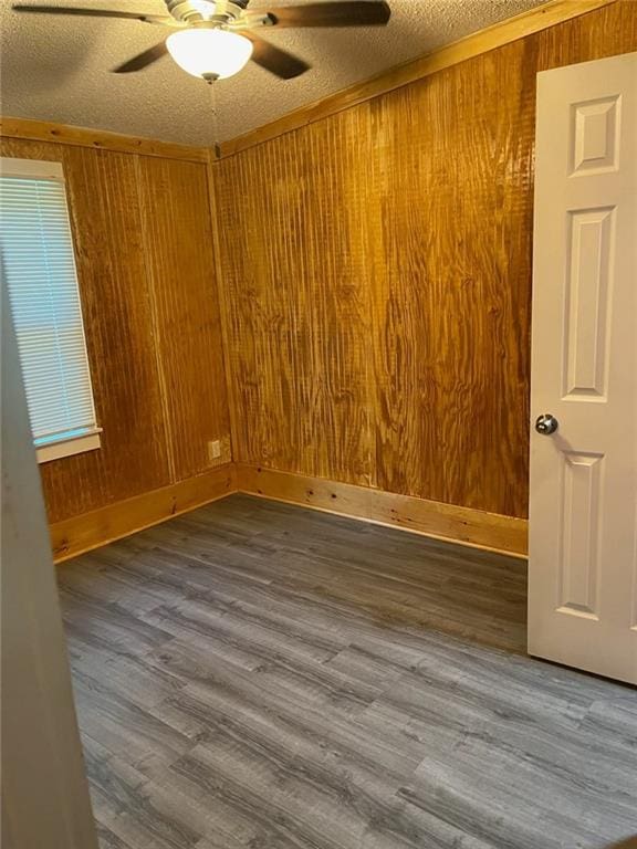 empty room featuring ceiling fan, a textured ceiling, wood walls, and wood-type flooring