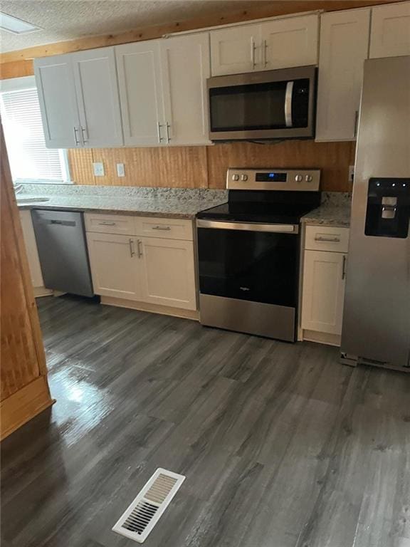 kitchen featuring light stone counters, white cabinets, appliances with stainless steel finishes, and dark wood-type flooring