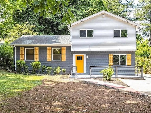 split level home featuring covered porch, brick siding, and a front yard