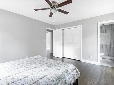bedroom with a closet, ensuite bath, ceiling fan, dark wood-style floors, and baseboards