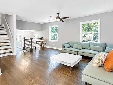 living room with plenty of natural light, stairway, a ceiling fan, and dark wood-style floors