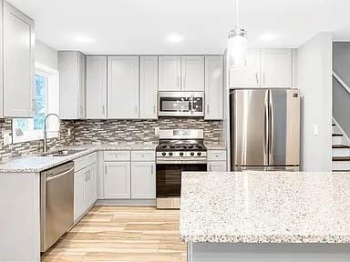 kitchen with a sink, stainless steel appliances, decorative backsplash, and light stone countertops