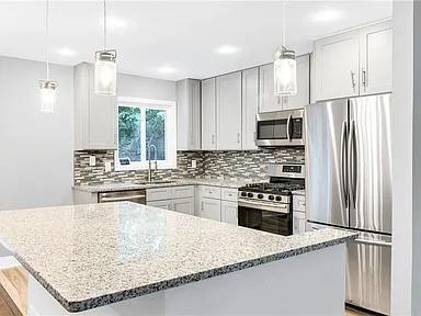 kitchen with hanging light fixtures, a sink, stainless steel appliances, light stone countertops, and backsplash