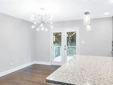 unfurnished dining area featuring french doors, a chandelier, dark wood-style flooring, and baseboards