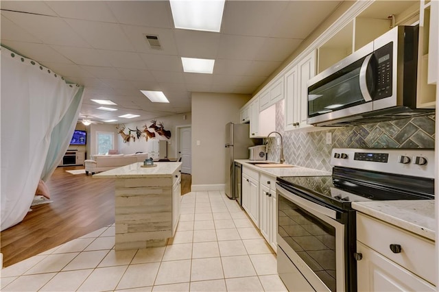 kitchen featuring a center island, sink, tasteful backsplash, light tile patterned floors, and appliances with stainless steel finishes