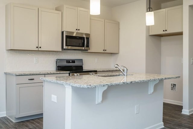 kitchen featuring a center island with sink, a sink, stainless steel appliances, decorative backsplash, and light stone countertops