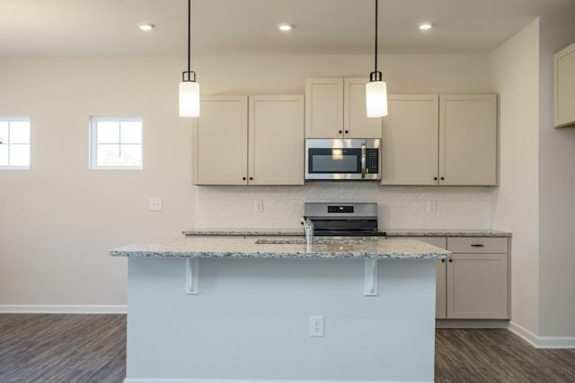 kitchen with light stone counters, baseboards, a kitchen island with sink, appliances with stainless steel finishes, and tasteful backsplash