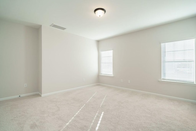 spare room featuring a wealth of natural light, visible vents, light carpet, and baseboards