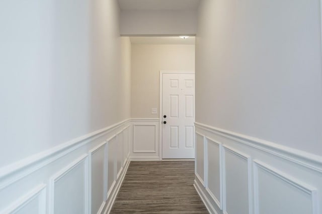 corridor with dark wood finished floors, a decorative wall, and a wainscoted wall