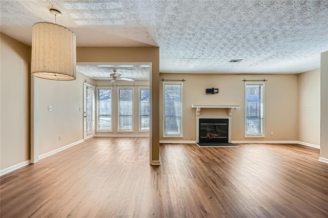 unfurnished living room with a glass covered fireplace, visible vents, a wealth of natural light, and wood finished floors