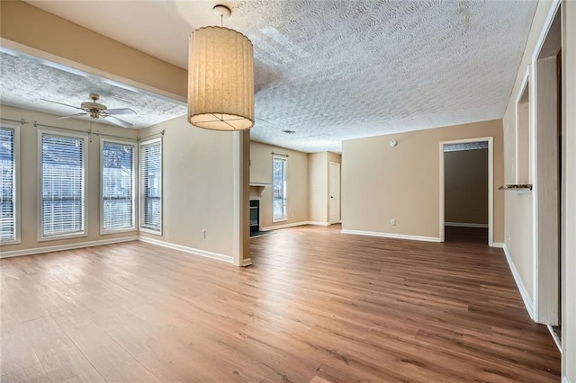 unfurnished living room featuring a fireplace, wood finished floors, baseboards, and a textured ceiling