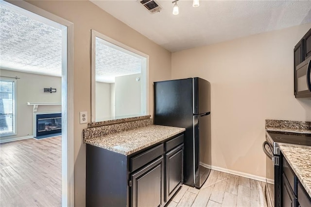 kitchen with baseboards, visible vents, light wood finished floors, black appliances, and a textured ceiling