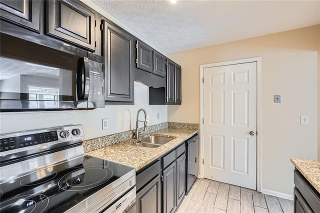 kitchen featuring black appliances, a sink, a textured ceiling, light stone countertops, and wood tiled floor