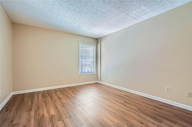 empty room with a textured ceiling, baseboards, and wood finished floors