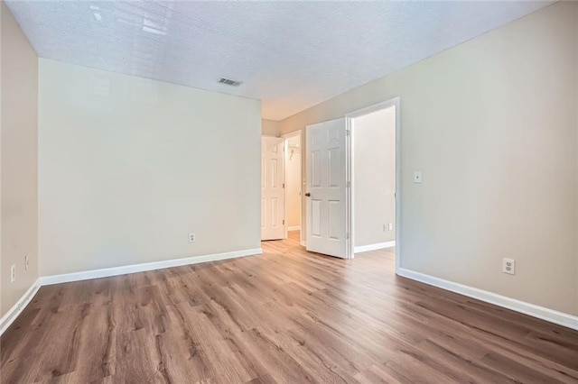 spare room with visible vents, baseboards, a textured ceiling, and wood finished floors