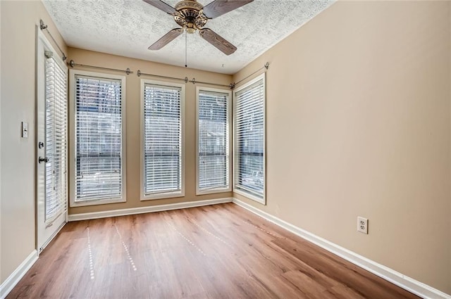 empty room with wood finished floors, baseboards, a textured ceiling, and ceiling fan