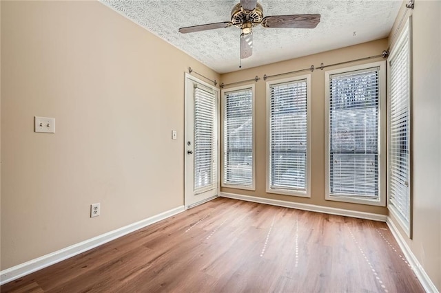 empty room with baseboards, plenty of natural light, a textured ceiling, and wood finished floors