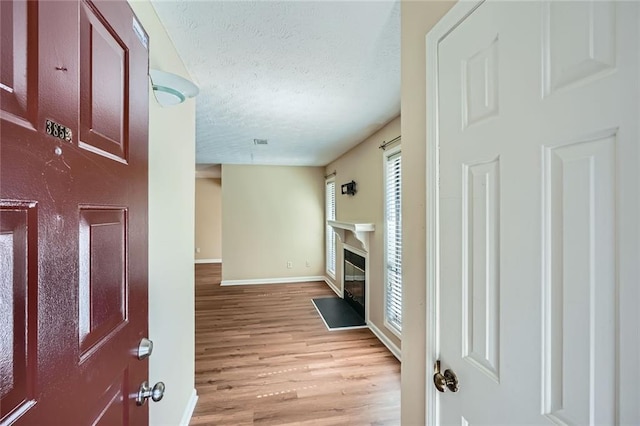 foyer featuring visible vents, a fireplace with flush hearth, a textured ceiling, light wood-style floors, and baseboards