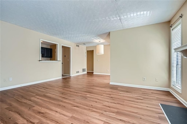 unfurnished living room featuring visible vents, baseboards, a textured ceiling, and wood finished floors