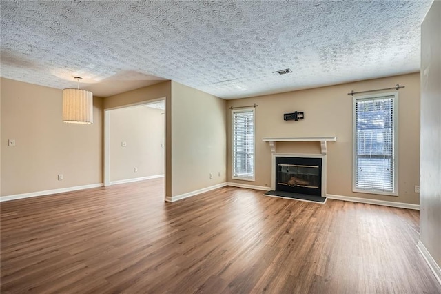 unfurnished living room with visible vents, a textured ceiling, a glass covered fireplace, wood finished floors, and baseboards