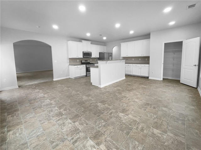 kitchen with tasteful backsplash, an island with sink, appliances with stainless steel finishes, and white cabinets