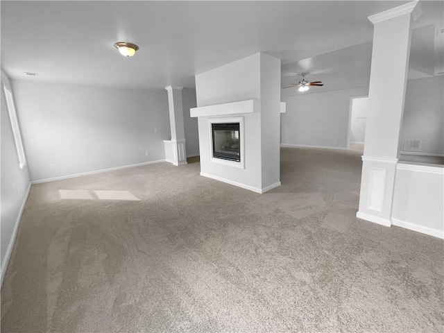 unfurnished living room featuring ceiling fan, a multi sided fireplace, carpet, and ornate columns