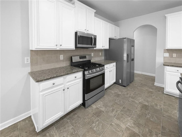 kitchen featuring decorative backsplash, stainless steel appliances, dark stone counters, and white cabinets