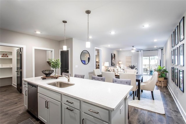 kitchen with stainless steel dishwasher, sink, dark hardwood / wood-style floors, hanging light fixtures, and an island with sink