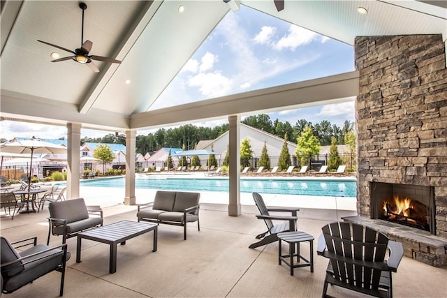 view of swimming pool with an outdoor stone fireplace, ceiling fan, and a patio area