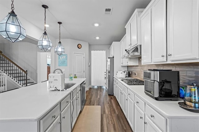 kitchen featuring pendant lighting, white cabinets, a center island with sink, tasteful backsplash, and stainless steel appliances