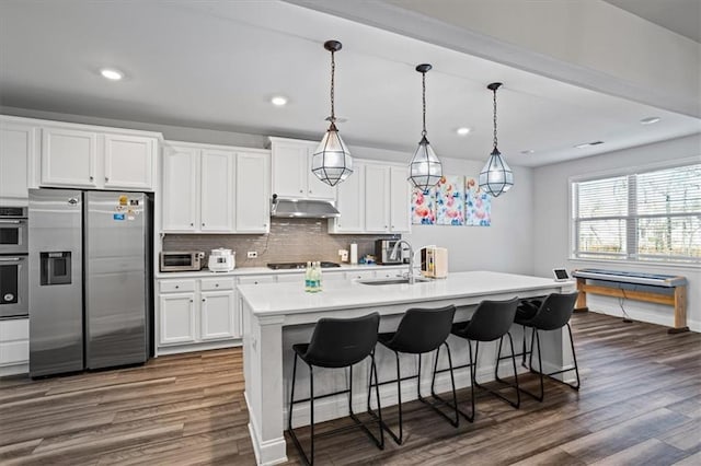 kitchen featuring a kitchen island with sink, white cabinets, sink, appliances with stainless steel finishes, and decorative light fixtures