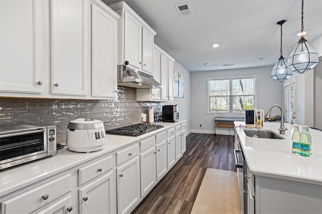 kitchen with backsplash, stainless steel gas cooktop, sink, decorative light fixtures, and white cabinets