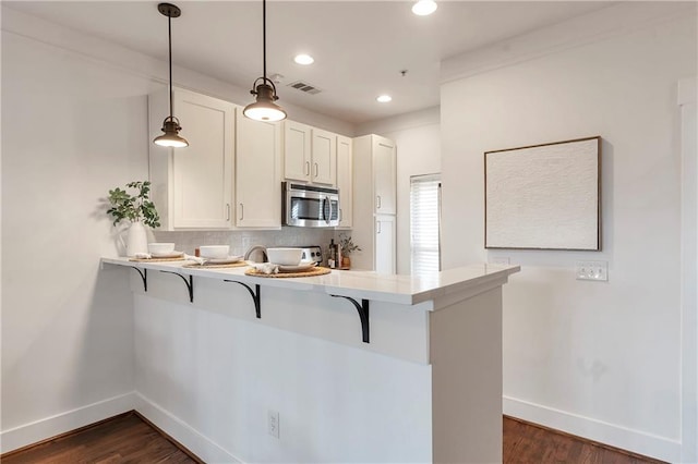 kitchen featuring kitchen peninsula, a breakfast bar, pendant lighting, white cabinets, and dark hardwood / wood-style floors