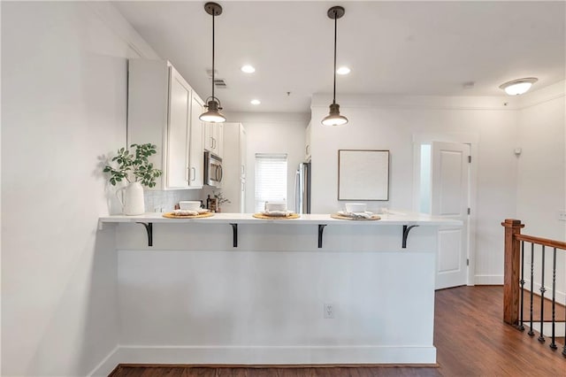 kitchen with kitchen peninsula, dark hardwood / wood-style floors, appliances with stainless steel finishes, white cabinetry, and a breakfast bar area