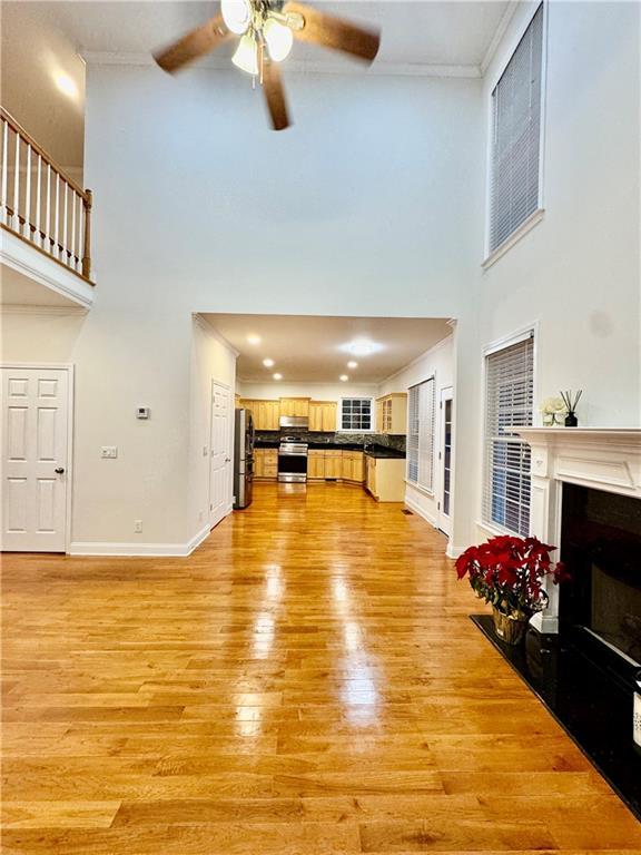 unfurnished living room featuring ceiling fan, light wood-type flooring, ornamental molding, and a towering ceiling