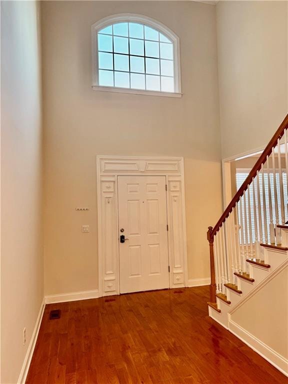 entryway with wood-type flooring and a towering ceiling