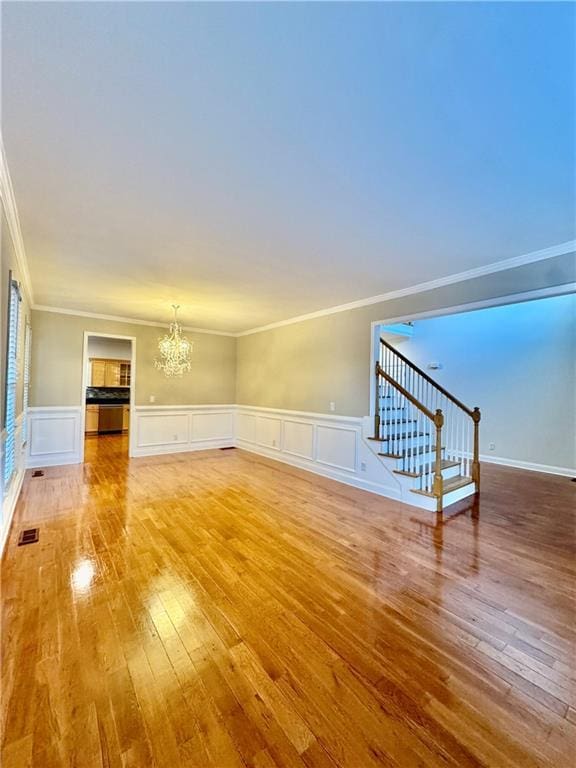 unfurnished living room featuring hardwood / wood-style flooring, crown molding, and an inviting chandelier