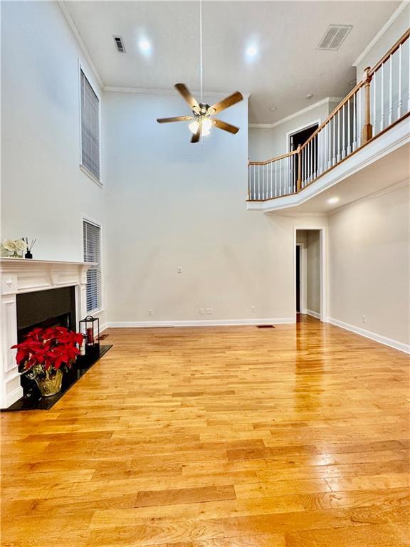 living room with a high ceiling, light hardwood / wood-style flooring, ceiling fan, and crown molding