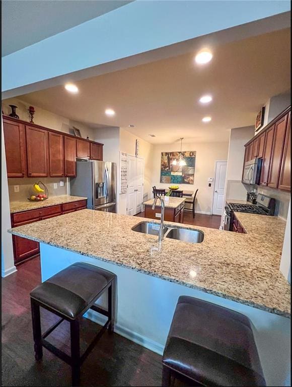 kitchen featuring kitchen peninsula, appliances with stainless steel finishes, a breakfast bar, sink, and decorative light fixtures