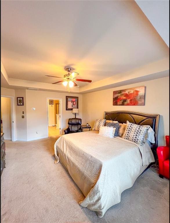 carpeted bedroom with a raised ceiling and ceiling fan