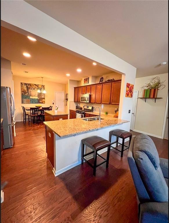 kitchen with light stone countertops, sink, stainless steel appliances, pendant lighting, and a breakfast bar area