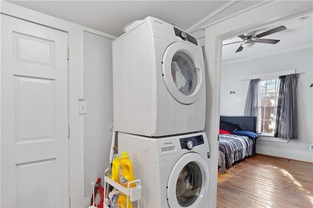 laundry room featuring hardwood / wood-style floors, a ceiling fan, laundry area, stacked washer and clothes dryer, and crown molding