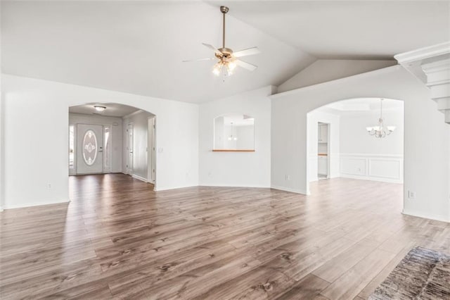 unfurnished living room featuring arched walkways, vaulted ceiling, wood finished floors, and ceiling fan with notable chandelier